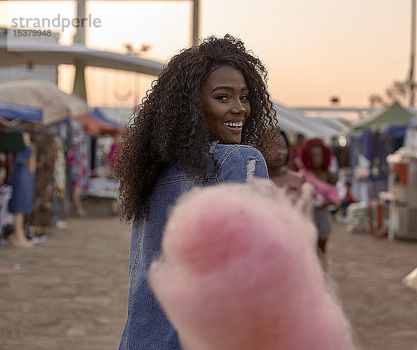 Porträt einer glücklichen jungen Frau mit rosa Zuckerwatte auf dem Strassenmarkt