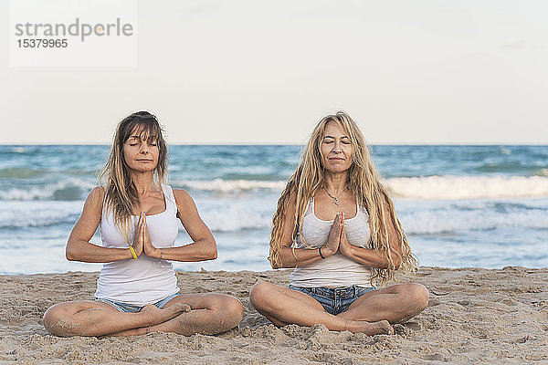 Zwei Frauen praktizieren Acro Yoga am Strand und meditieren