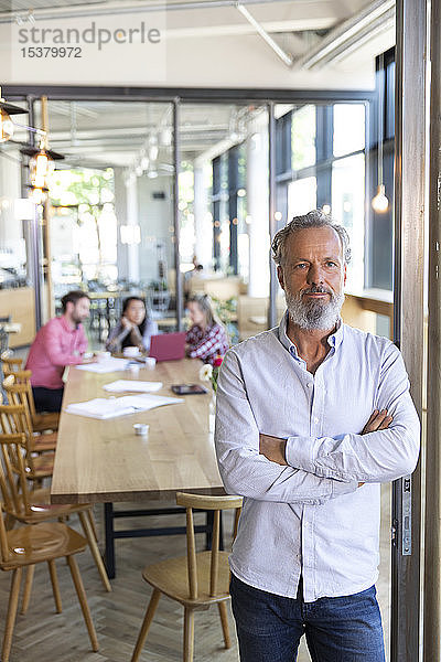 Porträt eines reifen Geschäftsmannes in einem Cafe mit Kollegen  die im Hintergrund eine Besprechung abhalten