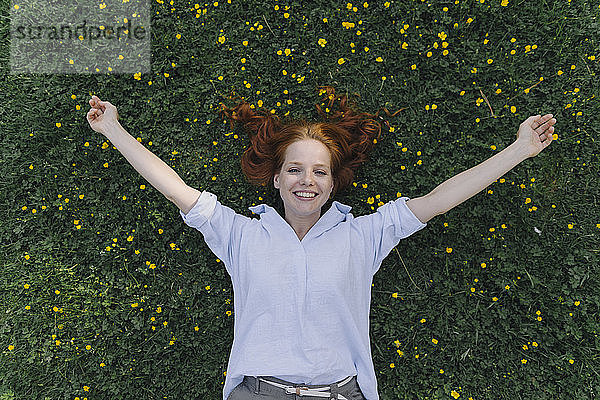 Porträt einer glücklichen rothaarigen Frau  die auf einer Blumenwiese liegt