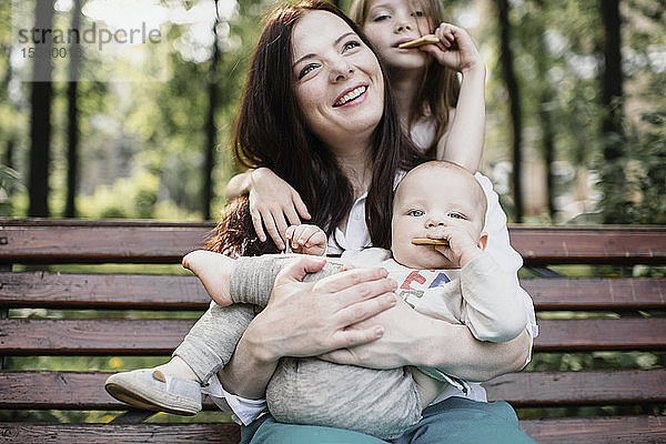 Lächelnde Mutter mit ihren beiden Kindern beim Keksessen im Park