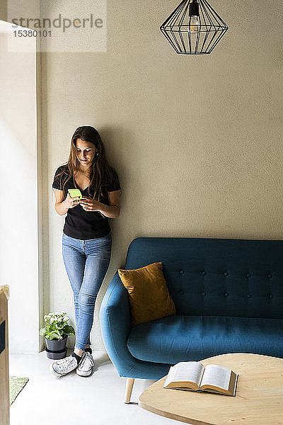 Junge Frau lehnt mit ihrem Handy an einer Wand