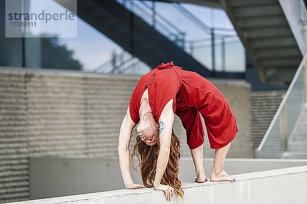 Sportliche junge Frau macht Akrobatik an einer Betonwand