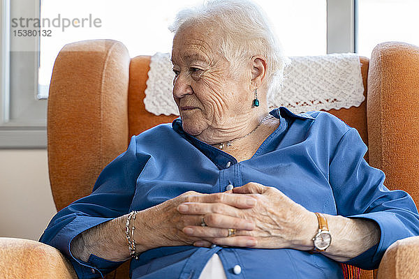 Ältere Frau sitzt in einem Sessel im Wohnzimmer