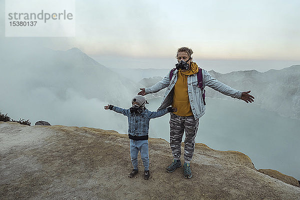 Vater und Sohn mit Atemschutzmasken stehen am Rande des Vulkans Ijen  Java  Indonesien