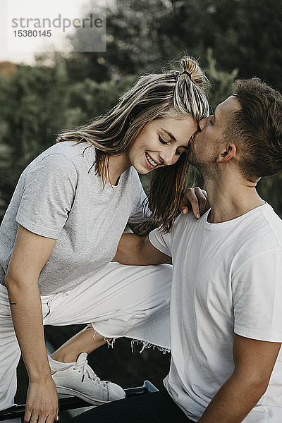 Porträt eines jungen lächelnden Paares  Mann küsst sie auf die Stirn