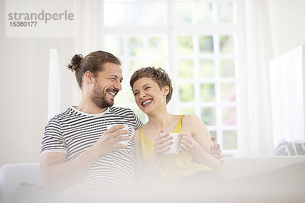 Glückliches junges Paar hält zu Hause Tassen auf der Couch