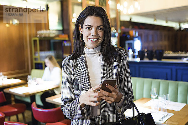 Porträt einer lächelnden Geschäftsfrau mit Handy in der Hand in einem Restaurant