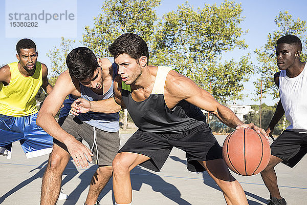 Junge Männer spielen Basketball und dribbeln Ball auf dem Sportplatz