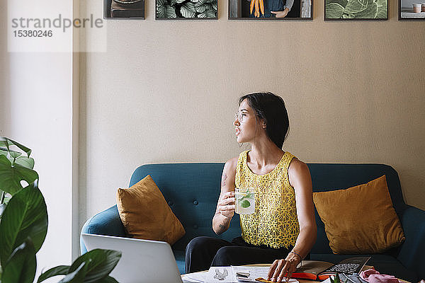 Modedesigner sitzt auf dem Sofa  macht eine Pause und trinkt aromatisiertes Wasser