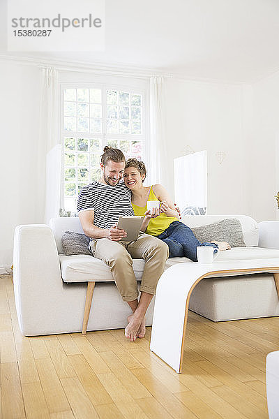 Glückliches junges Paar mit Tablette auf der Couch zu Hause