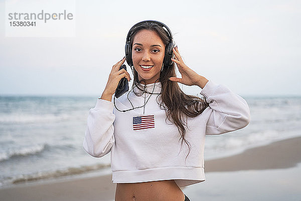 Porträt einer jungen Frau  die am Strand mit Kopfhörern Musik hört