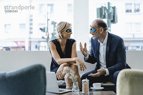 Geschäftsmann und -frau mit Superhelden-Masken  die eine Besprechung abhalten