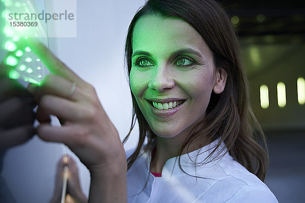 Nahaufnahme einer lächelnden Frau  die einen Touchscreen mit grüner LED berührt