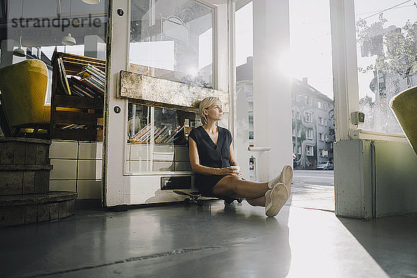 Geschäftsfrau im Café  sitzt auf einem Skateboard und entspannt