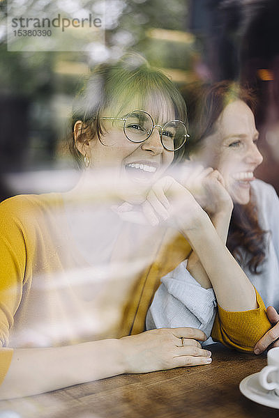 Zwei glückliche Freundinnen hinter einer Fensterscheibe in einem Cafe