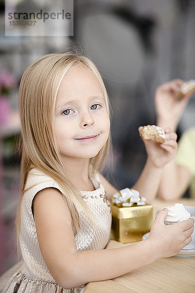 Porträt eines lächelnden kleinen Mädchens mit Geschenkkarton  das Kekse isst
