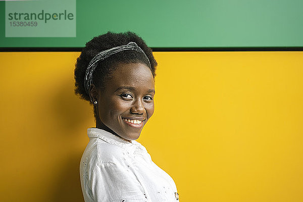 Porträt einer lächelnden jungen Frau vor gelber und grüner Wand