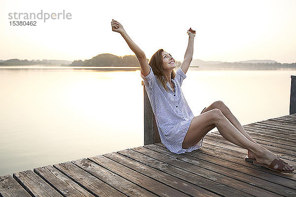 Glückliche reife Frau sitzt bei Sonnenaufgang auf einem Steg an einem See