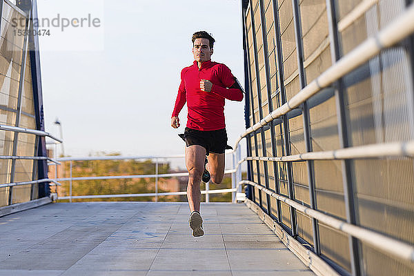 Jogger mit Smartphone in der Armtasche beim Laufen auf einer Brücke