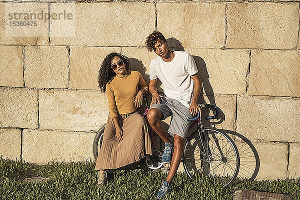 Junges Paar mit Fahrrad  an Steinmauer gelehnt  sieht cool aus