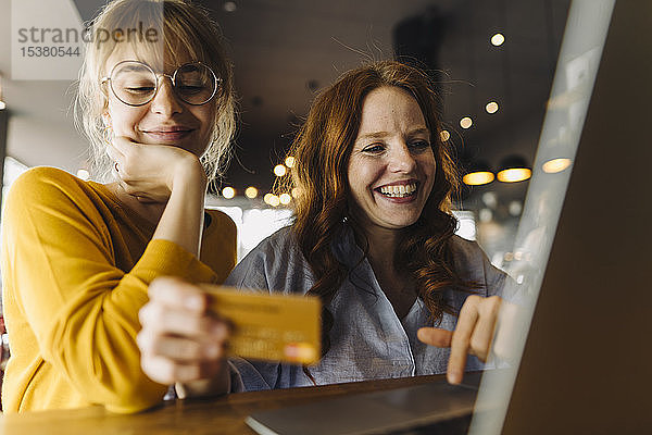 Zwei glückliche Freundinnen mit Laptop und Kreditkarte in einem Cafe