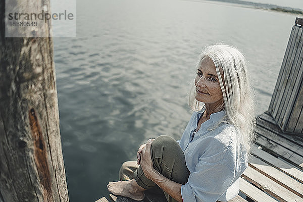 Ältere Frau sitzt auf einem Steg und entspannt sich am Meer