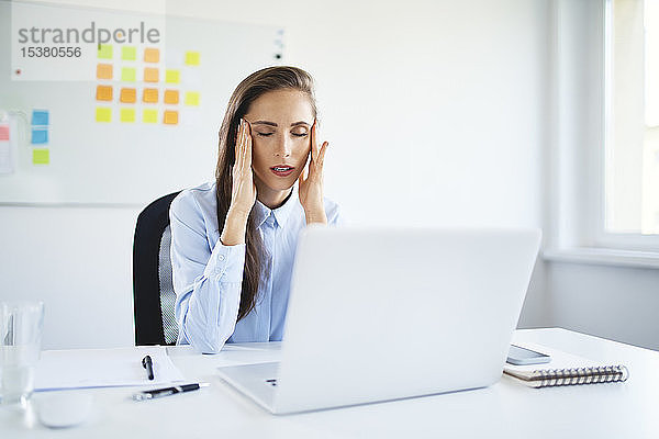 Junge Geschäftsfrau sitzt im Büro und leidet unter Kopfschmerzen