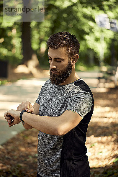 Sportlicher Mann im Wald bei der Kontrolle seiner Smartwatch