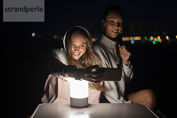 Zwei Freundinnen mit LED-Licht auf dem Campingtisch beim nächtlichen Selfie