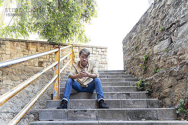 Mann sitzt auf einer Außentreppe und benutzt ein Mobiltelefon