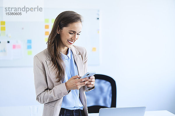 Lächelnde Geschäftsfrau steht mit Smartphone im Büro