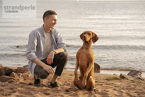 Junger Mann mit seinem Hund beim Training am Strand