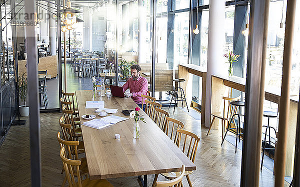 Junger Mann mit Laptop am Holztisch in einem Café