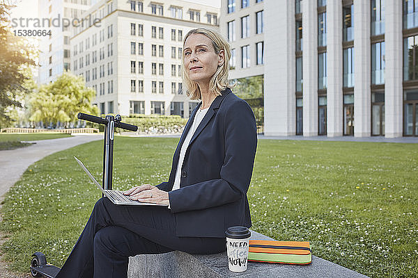 Geschäftsfrau  die in der Stadt mit einem Laptop an einer Wand sitzt