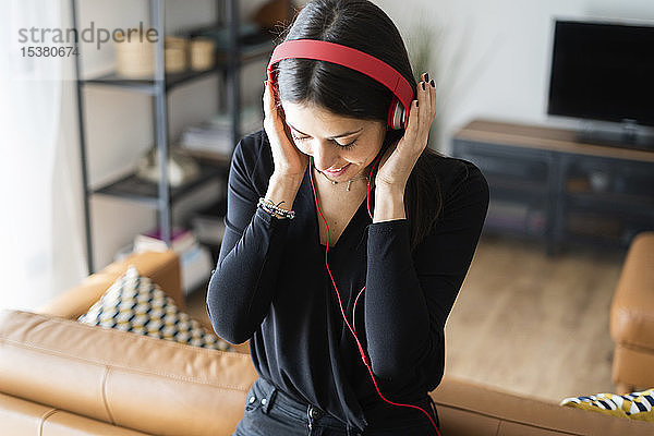 Lächelnde junge Frau  die zu Hause mit Kopfhörern Musik hört
