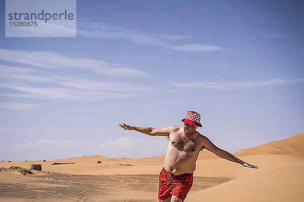 Glücklicher übergewichtiger Mann mit Badeshorts läuft in der Wüste von Marokko
