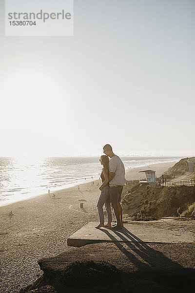 Liebenswertes junges Paar genießt den Blick auf den Strand bei Sonnenuntergang