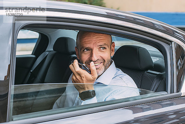 Geschäftsmann  der auf dem Rücksitz eines Autos sitzt  ein Smartphone benutzt und sich umsieht