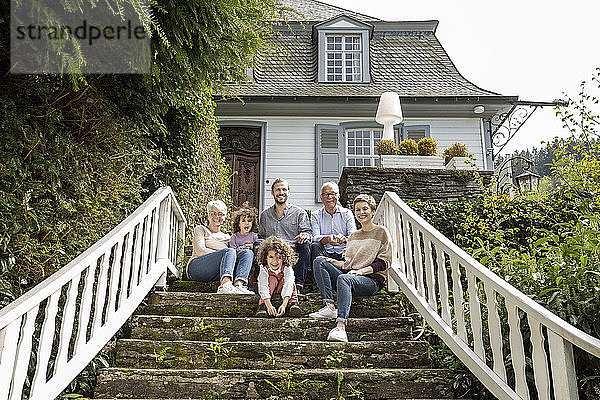 Glückliche Großfamilie  die auf einer Treppe im Garten ihres Hauses sitzt