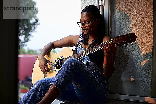 Am Fensterrand sitzende  Gitarre spielende Frau