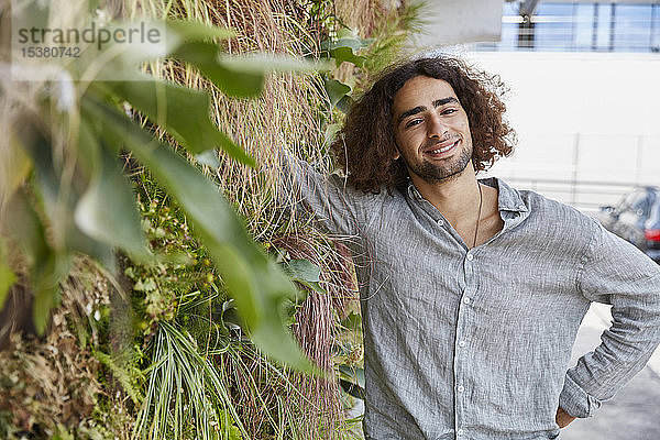 Porträt eines lächelnden jungen Mannes vor einer Pflanzenwand