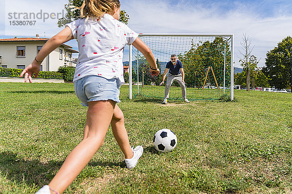Vater und Tochter spielen auf einer Wiese Fussball
