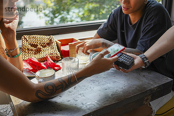 Junge Frau bezahlt Rechnung mit Smartphone im Café
