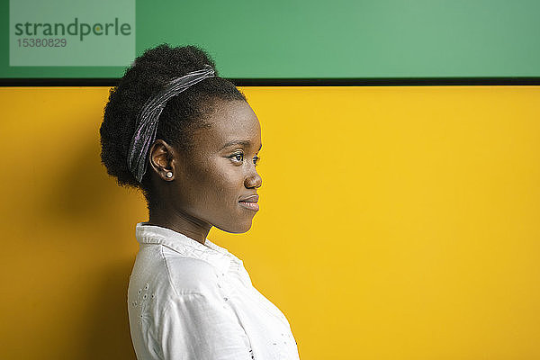 Porträt einer jungen Frau vor gelber und grüner Wand  die in die Ferne schaut