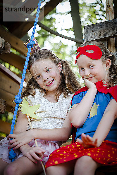 Als Prinzessin und Superwoman verkleidete Mädchen spielen in einem Baumhaus