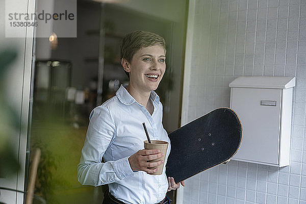 Glückliche Geschäftsfrau hält Tasse und Skateboard