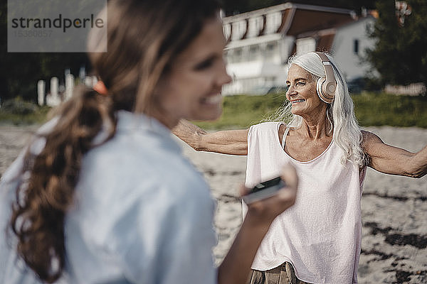 ältere Frau tanzt am Strand  Tochter lacht im Vordergrund