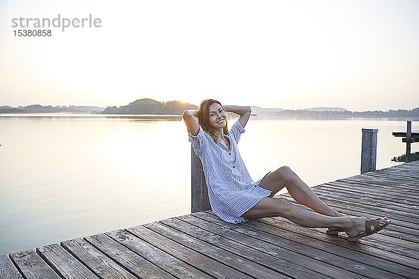Porträt einer reifen Frau  die bei Sonnenaufgang auf einem Steg an einem See sitzt