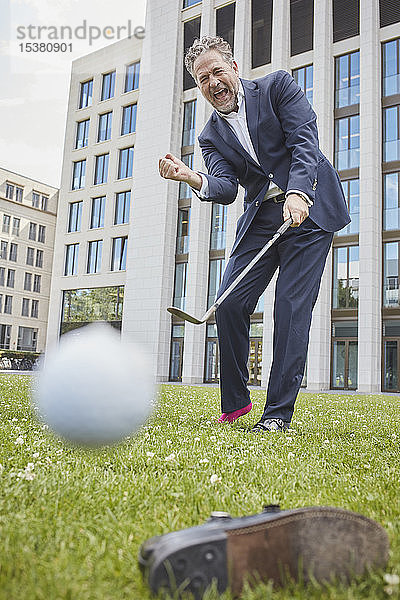 Glücklicher reifer Geschäftsmann spielt Golf auf dem Rasen in der Stadt